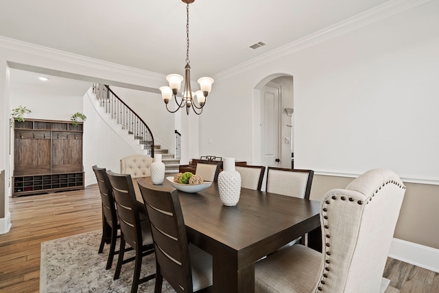 dining space featuring ornamental molding, light wood finished floors, a chandelier, arched walkways, and stairs
