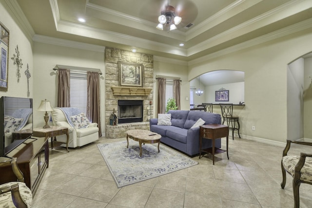 living area with arched walkways, ceiling fan, a stone fireplace, a raised ceiling, and light tile patterned floors