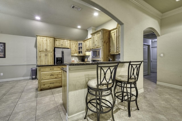 kitchen featuring stainless steel appliances, arched walkways, dark countertops, a peninsula, and light tile patterned floors