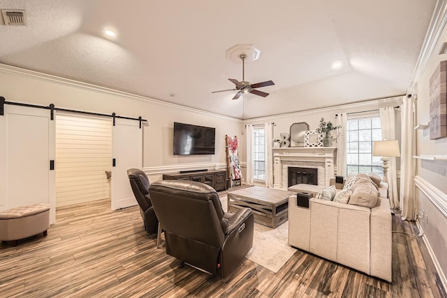 living area with a barn door, wood finished floors, a stone fireplace, a ceiling fan, and plenty of natural light