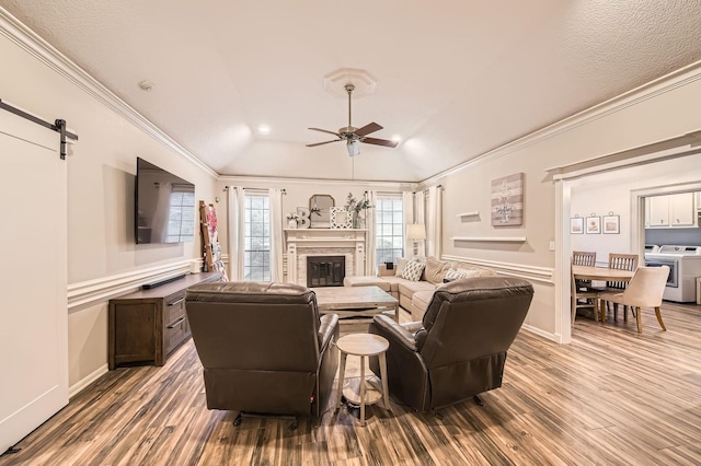 living area with washing machine and clothes dryer, wood finished floors, a ceiling fan, a glass covered fireplace, and ornamental molding