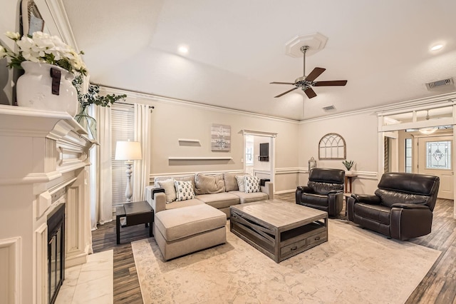 living area with wood finished floors, a ceiling fan, a fireplace, ornamental molding, and lofted ceiling