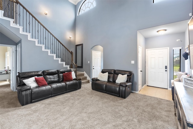 living room with light carpet, a towering ceiling, stairs, arched walkways, and baseboards