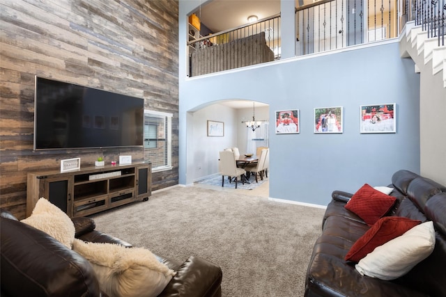 carpeted living area featuring a high ceiling, arched walkways, a chandelier, and baseboards
