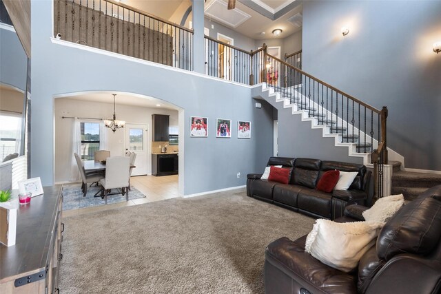 carpeted living room featuring a towering ceiling, a chandelier, arched walkways, baseboards, and stairway