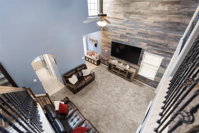 carpeted living room with ceiling fan, arched walkways, and a towering ceiling