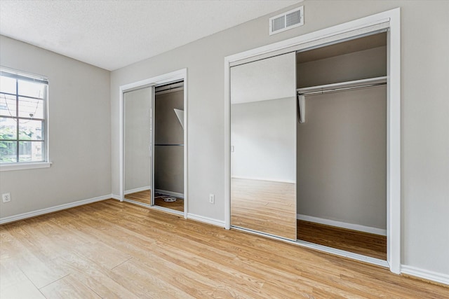 unfurnished bedroom featuring two closets, wood finished floors, baseboards, and a textured ceiling