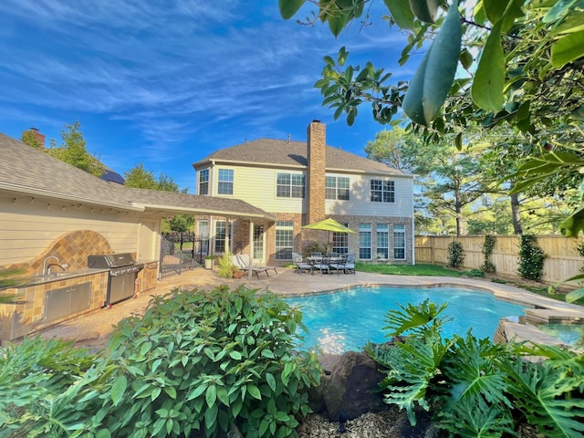 view of pool featuring an outdoor kitchen, a fenced backyard, area for grilling, a patio area, and a sink