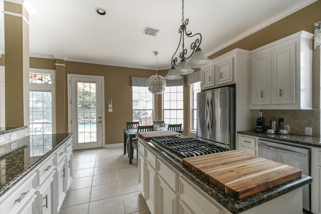 kitchen featuring appliances with stainless steel finishes, a center island, decorative backsplash, ornamental molding, and hanging light fixtures