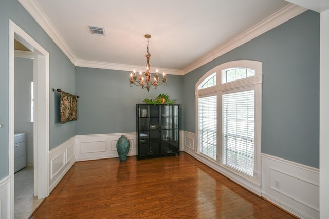 unfurnished dining area with a chandelier, crown molding, a wainscoted wall, a decorative wall, and wood finished floors