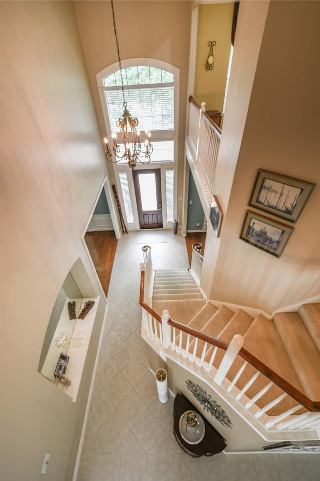 entryway with a high ceiling, tile patterned flooring, a chandelier, baseboards, and stairs