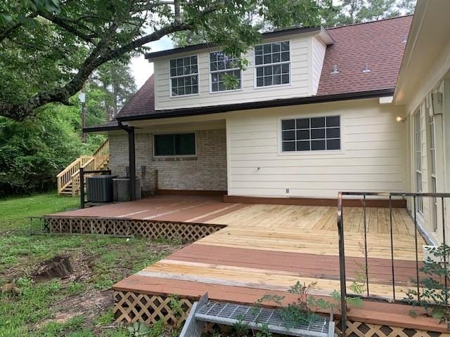 rear view of property with a deck, stairway, central AC unit, brick siding, and a shingled roof