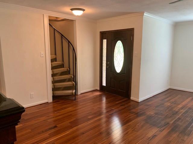 entryway featuring wood finished floors, ornamental molding, stairs, and baseboards