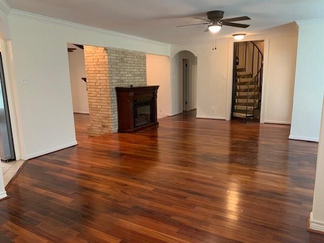unfurnished living room with ceiling fan, arched walkways, stairway, hardwood / wood-style floors, and a glass covered fireplace