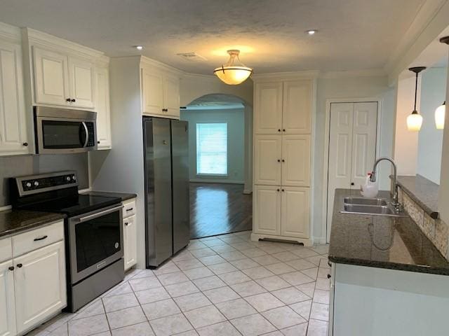 kitchen with appliances with stainless steel finishes, a sink, arched walkways, light tile patterned floors, and white cabinets