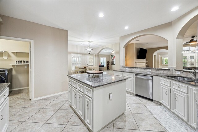kitchen featuring stainless steel dishwasher, a sink, arched walkways, light stone countertops, and recessed lighting