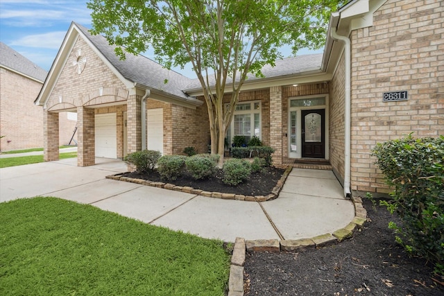entrance to property featuring driveway, brick siding, roof with shingles, and a garage