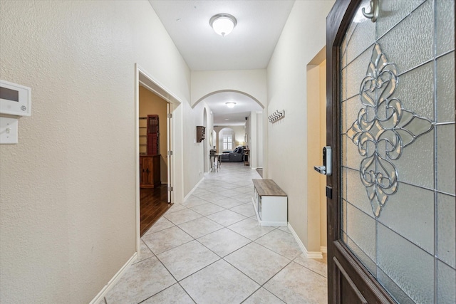 corridor featuring arched walkways, light tile patterned floors, and baseboards