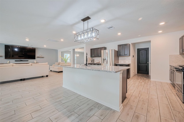 20864 Sheffield Park Dr, Porter, TX 77365 - kitchen with stainless steel refrigerator with ice dispenser, wood finish floors, light stone countertops, hanging light fixtures, and a center island with sink