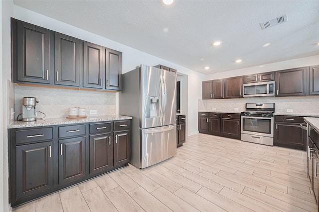 20864 Sheffield Park Dr, Porter, TX 77365 - kitchen featuring stainless steel appliances, backsplash, dark brown cabinetry, a textured ceiling, and light stone countertops