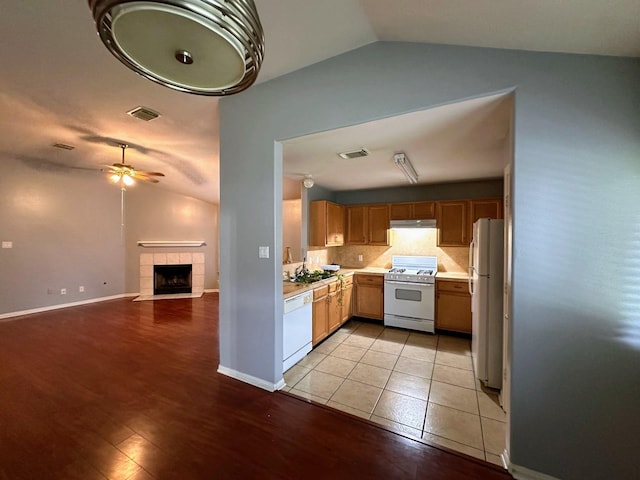 kitchen featuring white appliances, lofted ceiling, light countertops, a ceiling fan, and a fireplace