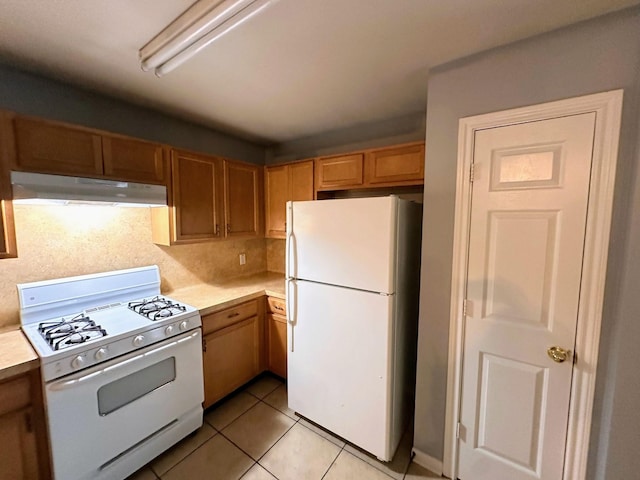 kitchen featuring white appliances, under cabinet range hood, light countertops, and light tile patterned floors