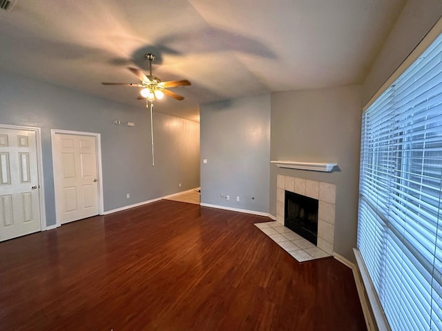 unfurnished living room with a ceiling fan, wood finished floors, a tile fireplace, and baseboards