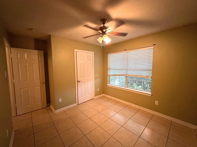 unfurnished bedroom with light tile patterned floors, a textured ceiling, baseboards, and ceiling fan