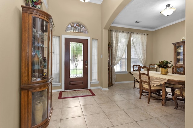 entrance foyer featuring arched walkways, ornamental molding, light tile patterned floors, and baseboards