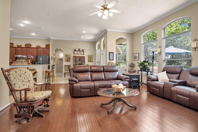 living room featuring arched walkways, a ceiling fan, recessed lighting, light wood-style flooring, and baseboards
