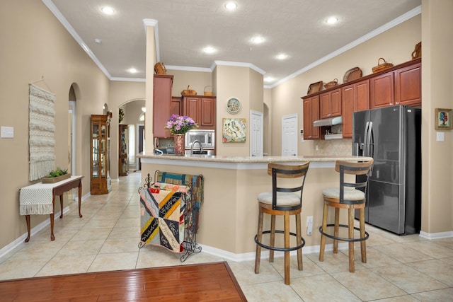 kitchen featuring stainless steel appliances, arched walkways, under cabinet range hood, ornamental molding, and backsplash