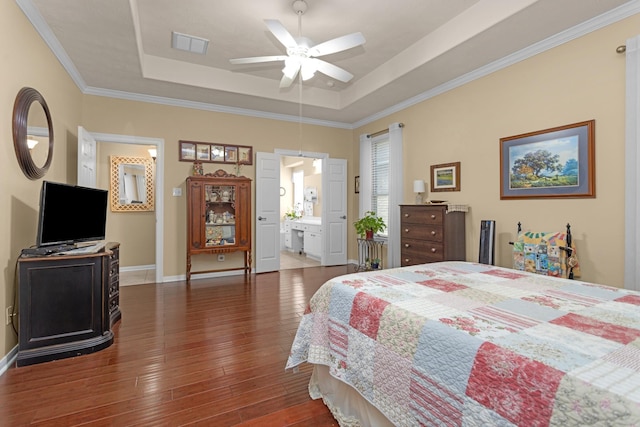 bedroom featuring a tray ceiling, hardwood / wood-style floors, baseboards, ornamental molding, and ensuite bathroom