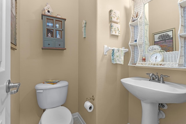 half bathroom with toilet, baseboards, and a sink