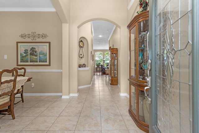 entrance foyer featuring arched walkways, baseboards, ornamental molding, and light tile patterned flooring