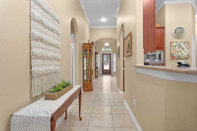 hallway with arched walkways, crown molding, light tile patterned floors, and baseboards