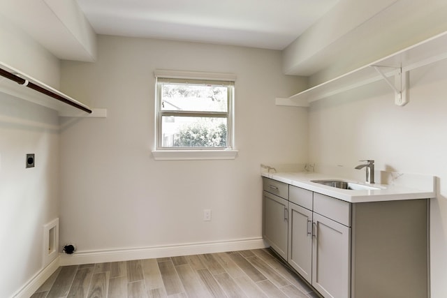 laundry room featuring electric dryer hookup, light wood-type flooring, baseboards, and cabinet space