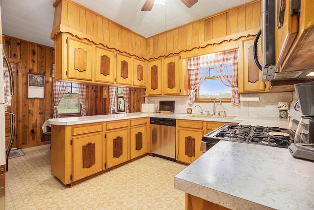 kitchen with appliances with stainless steel finishes, a sink, light countertops, a peninsula, and wooden walls