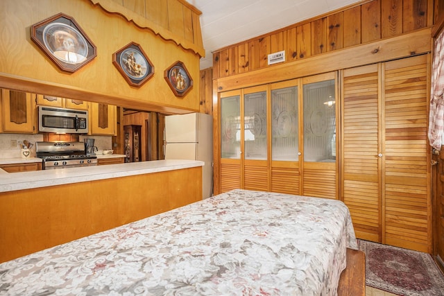 bedroom featuring wooden walls and freestanding refrigerator