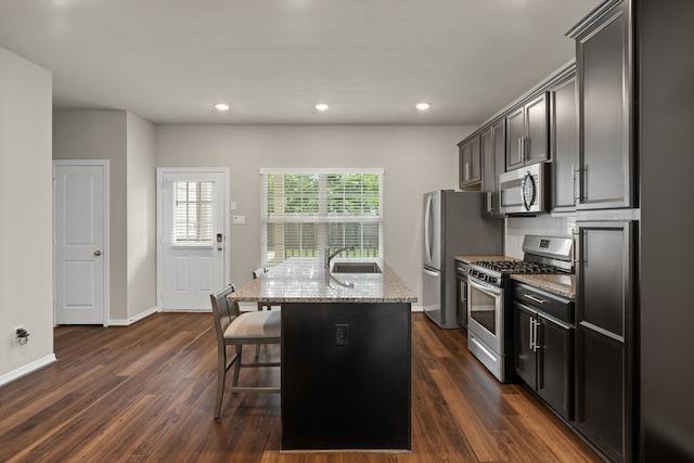 kitchen featuring stainless steel appliances, a sink, light stone counters, an island with sink, and healthy amount of natural light