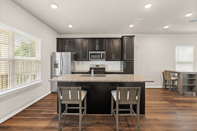 kitchen featuring stainless steel appliances, a center island with sink, dark wood finished floors, baseboards, and a breakfast bar area