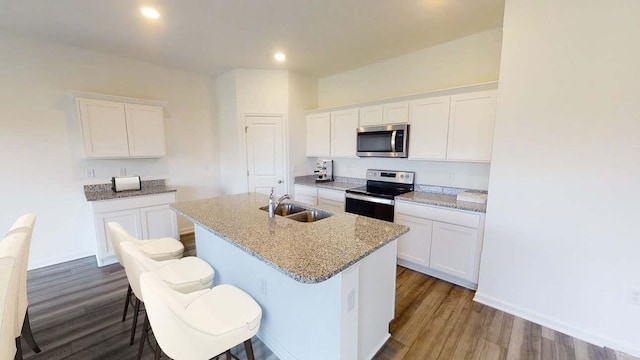 15311 Abella Dr, Montgomery, TX 77316 - kitchen with stainless steel appliances, a sink, a center island with sink, wood finished floors, and white cabinetry