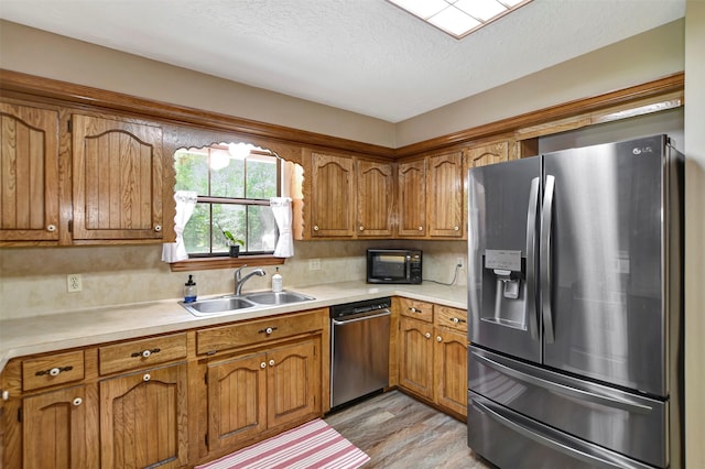 26410 Anderson Rd, Magnolia, TX 77354 - kitchen with appliances with stainless steel finishes, a sink, brown cabinets, light wood-type flooring, and light countertops