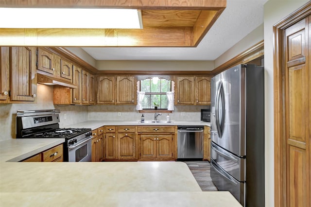 26410 Anderson Rd, Magnolia, TX 77354 - kitchen featuring stainless steel appliances, under cabinet range hood, light countertops, a sink, and brown cabinetry