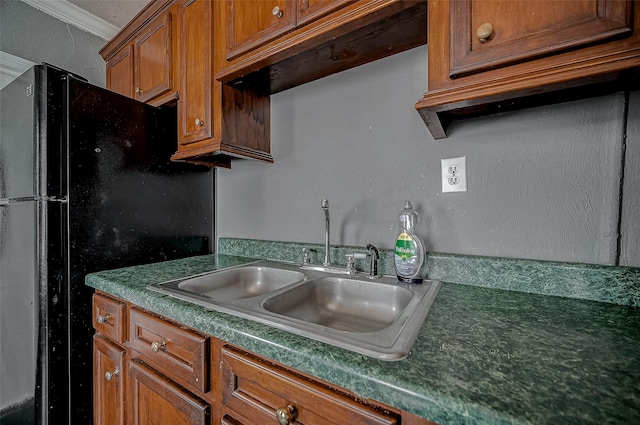 kitchen featuring a sink, brown cabinetry, freestanding refrigerator, dark countertops, and ornamental molding