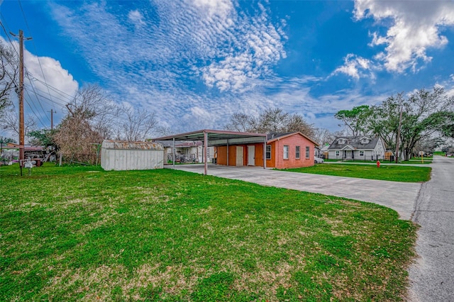 view of front facade with concrete driveway, a front yard, a carport, a storage unit, and an outbuilding