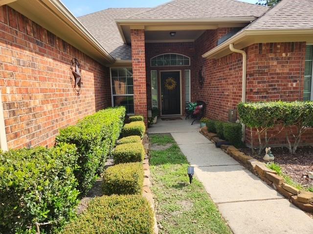 entrance to property featuring a shingled roof and brick siding