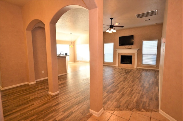 unfurnished living room with arched walkways, a ceiling fan, wood finished floors, a fireplace, and baseboards