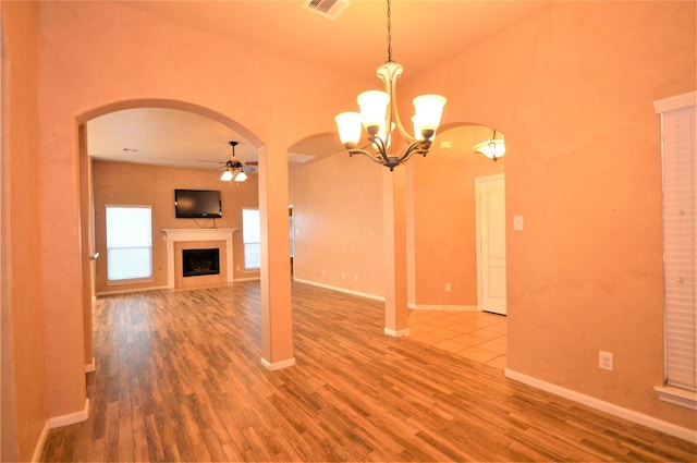 unfurnished living room with arched walkways, wood finished floors, a ceiling fan, and a fireplace