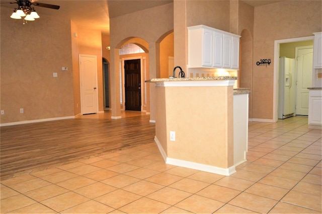 kitchen featuring arched walkways, white fridge with ice dispenser, a ceiling fan, white cabinetry, and baseboards