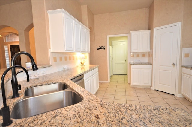 kitchen with a sink, arched walkways, light tile patterned floors, backsplash, and white cabinets